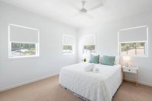 a white bedroom with a bed with two windows at Biirinba Top Floor - oceanstays in Yamba