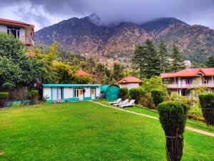 a green yard with houses and a mountain in the background at Gagan Resorts in Dharamshala