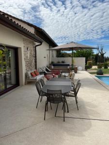 um pátio com uma mesa, cadeiras e um guarda-sol em Le Vieux Platane em Malissard