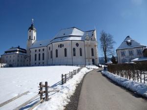 un grand bâtiment blanc dans la neige avec une clôture dans l'établissement Bergkiefer - Ferienwohnung, à Oy-Mittelberg