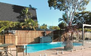 a swimming pool with a table and chairs and a fence at Admiral Nelson Motor Inn in Nelson Bay