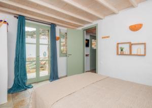 a bedroom with a bed and a window with blue curtains at Houses at Chrisopigi Sifnos in Chrisopigi