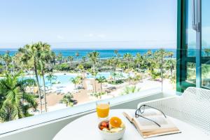 a table with a bowl of fruit and a glass of orange juice and the ocean at Parque Santiago IV Official in Playa de las Americas
