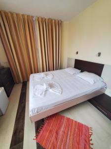 a bedroom with a bed with white sheets and a rug at Coral Guest House in Obzor