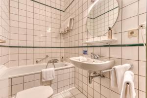 een wit betegelde badkamer met een wastafel en een toilet bij Hôtel Le Cor de Chasse in Saint-Hubert