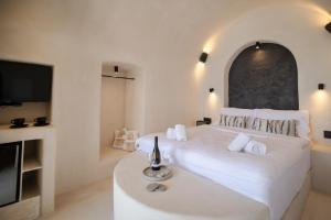 a white bedroom with a large bed and a tv at One of One - Aether in Oia