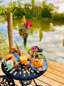 een tafel met ontbijtproducten en drankjes op een tafel bij het water bij Cottage, Lodge & Spa in Prouilly