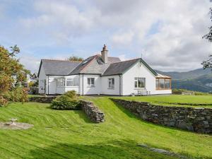 uma casa branca com uma parede de pedra e relva verde em Cae-fadog Fach em Barmouth