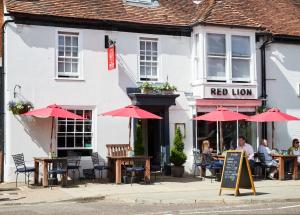 um restaurante com mesas e guarda-sóis em frente a um edifício em The Red Lion em Odiham