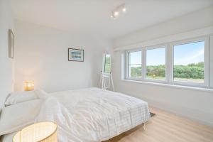 een witte slaapkamer met een bed en 2 ramen bij maison des dunes in Oostende