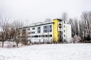 een geel en wit gebouw in de sneeuw bij B&B HOTEL München-Airport in Hallbergmoos