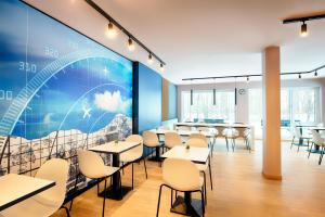 a dining room with tables and chairs and a large mural at B&B HOTEL München-Airport in Hallbergmoos