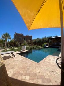 a large swimming pool with a yellow umbrella at Dar Lily, villa familiale avec piscine et services in Skoura