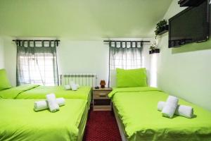 two beds in a room with green sheets and a tv at Hostel Aurora in Požarevac