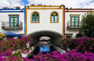 un edificio con un corso d'acqua di fronte ad esso con fiori viola di APARTAMENTO BONITO 103 a Playa del Ingles