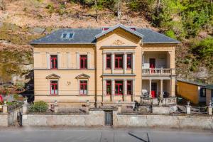 Una gran casa amarilla con ventanas rojas en una colina en Villa Emma, Wellness & Ayurveda, en Bad Schandau