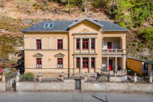 a large yellow house with red windows on a hill at Villa Emma, Wellness & Ayurveda in Bad Schandau