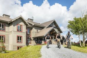 three people riding bikes in front of a house at Auberge de Montagne des Chic-Chocs Mountain Lodge - Sepaq in Sainte-Anne-des-Monts