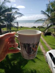 a person holding a coffee cup in front of a window at casa de praia a beira mar in Campina
