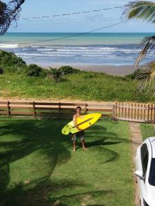 a man holding a yellow surfboard in front of a beach at casa de praia a beira mar in Campina