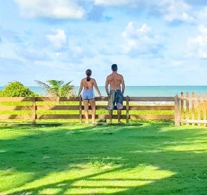 a man and woman standing on a fence looking at the ocean at casa de praia a beira mar in Campina