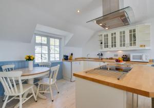cocina con armarios blancos, mesa y sillas en Cliff Top Cottage en Porthleven