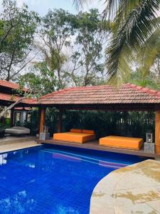 a swimming pool with a gazebo with orange benches at The Postcard Saligao in Calangute