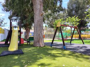 un parc avec deux balançoires et un arbre dans l'établissement Camping El Jardín, à El Campello