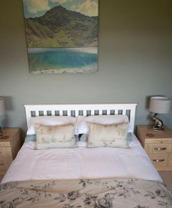 a white bed with pillows and a painting on the wall at Cae Glas in Penmaen-mawr