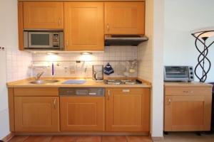 eine Küche mit Holzschränken, einer Spüle und einer Mikrowelle in der Unterkunft Strandstraße 16 - Wohnung 33 / 9877 in Kühlungsborn