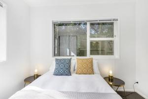 a white bedroom with a bed and two tables at Coastal Calm is near to the Beach with BBQ in Auckland