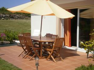 una mesa de madera y sillas con sombrilla en el patio en Gite bord de mer jacuzzi en Plougrescant