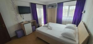 a bedroom with a white bed with purple curtains at Pensiunea Casa Beatrice in 2 Mai +23 photos