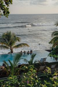 a swimming pool next to the ocean with people in it at Puro Surf Hotel in El Zonte