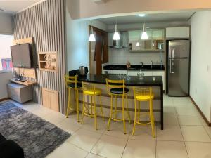 a kitchen with a bar with yellow stools in it at Apartamento Condado de Majorca in Capão da Canoa