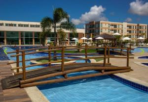 a resort swimming pool with wooden benches and umbrellas at Maraújosflat, Porto de Galinhas in Porto De Galinhas