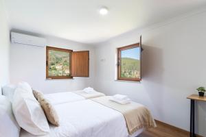 a white bedroom with a bed and two windows at NEW - Casa das Domingas in Vide