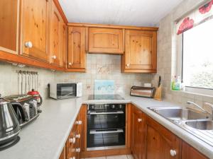 cocina con armarios de madera, fregadero y microondas en Beech Cottage en Ulverston
