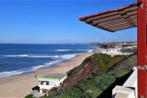 a view of a beach with a red building and the ocean at Pé na Praia in Torres Vedras +15 photos