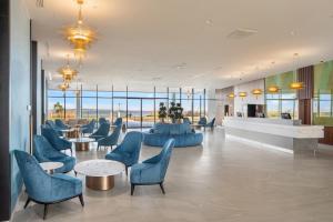 un vestíbulo con sillas azules, mesas y ventanas en Sirius Hotel****Superior, en Keszthely