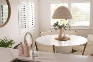 a white dining room with a table and a lamp at Mirage Luxury Beachside 3 Bedroom Apartment in Alexandra Headland