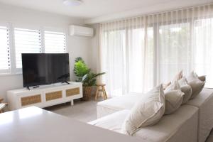 a living room with a white couch and a flat screen tv at Mirage Luxury Beachside 3 Bedroom Apartment in Alexandra Headland