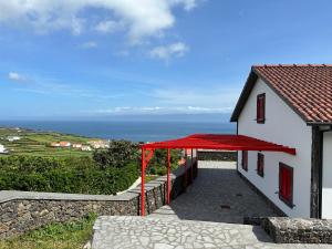 een wit huis met een rood dak en de oceaan bij Adega do Cachalote in Prainha de Baixo