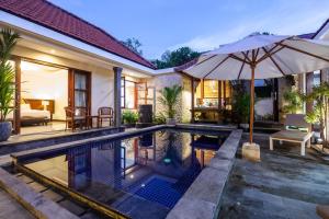 an outdoor swimming pool with an umbrella next to a house at Sanur Beach Villa - 3BR Private Pool in Sanur
