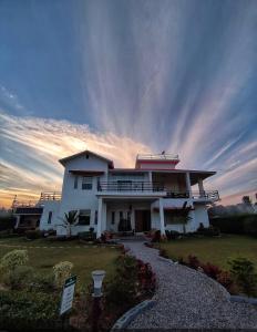 a large white house with a sunset in the background at Hriday Bhoomi - Luxury Cottages & Villa in Jim Corbett in Jhirna