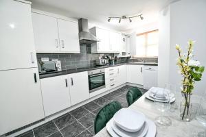 a kitchen with white cabinets and a table with green chairs at George Stephenson 1 mile from North Tees Hospital in Stockton-on-Tees