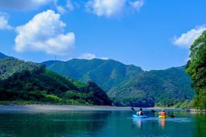 three people kayaking on a river with mountains in the background at 四万十川まで歩いて行ける 一棟まるっと貸し切りの宿 gu in Shimanto