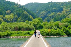 two people walking on a bridge over a river at 四万十川まで歩いて行ける 一棟まるっと貸し切りの宿 gu in Shimanto