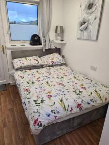 a bedroom with a bed with a floral comforter and a window at Sunset Place in Lower Boscaswell