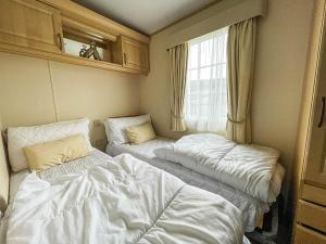 Duas camas num pequeno quarto com uma janela em Beautiful Caravan At Manor Park In Hunstanton Beach, Norfolk Ref 23026h em Hunstanton